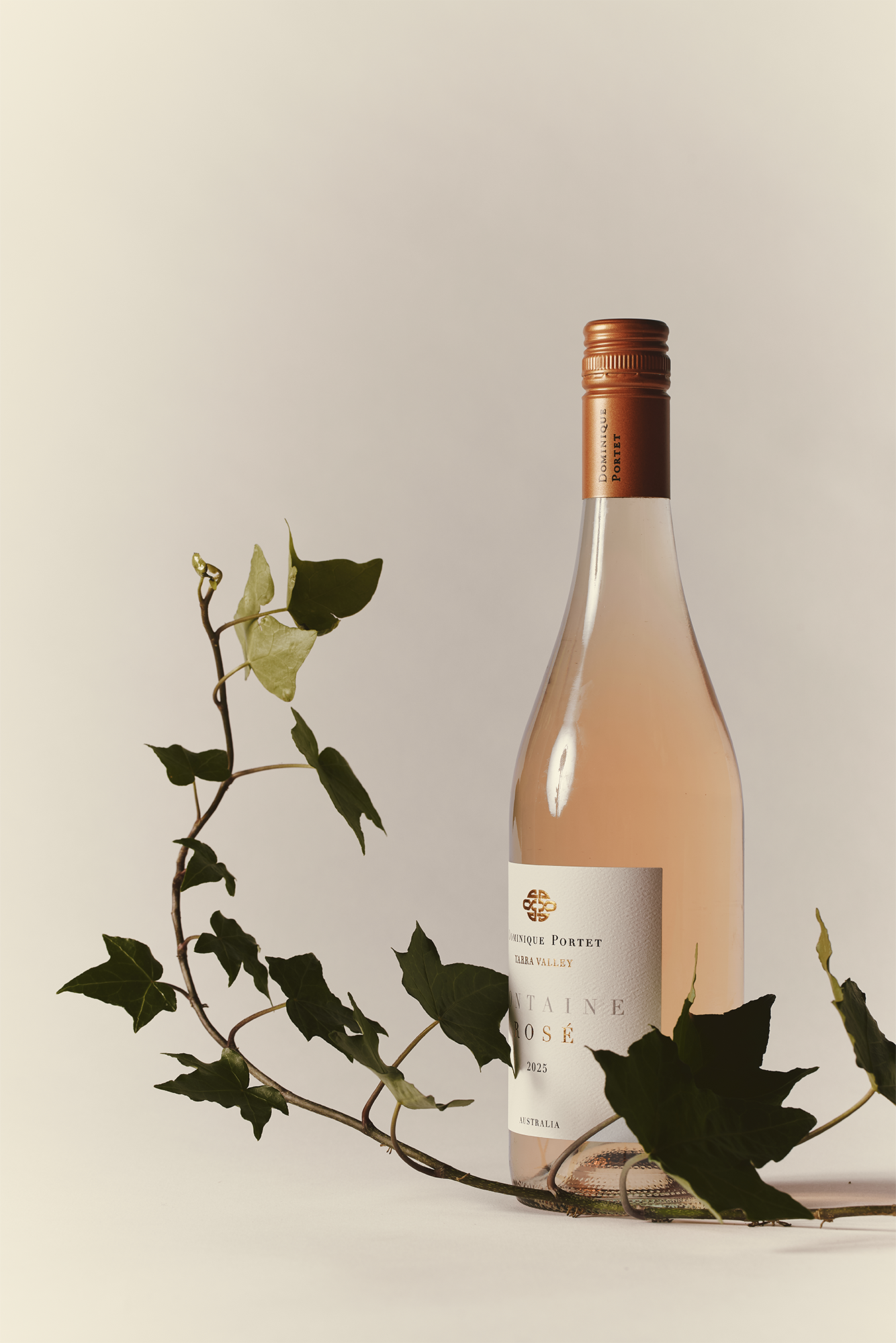 A bottle of rosé wine with a copper-colored cap stands next to green ivy leaves, set against a light beige background. The wine label reads “Château Mosé” with elegant, minimal design.